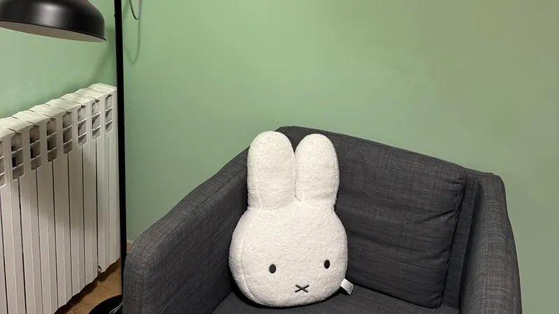 Fotelja sa zečjim jastukom i podna lampa uz zeleni zid u kabinetu